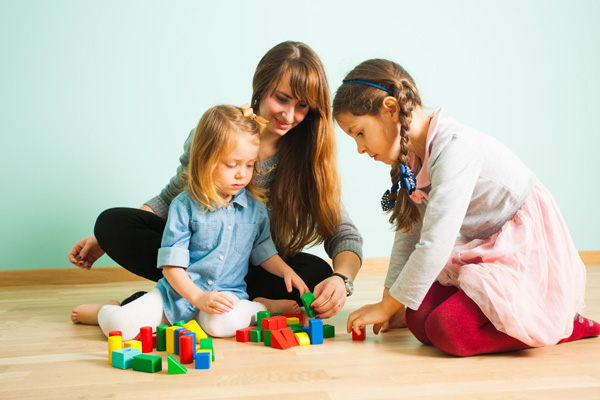 Young nanny playing with kids while babysitting